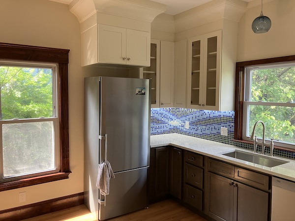 Left-hand view of a kitchen with new appliances, hardwood floor, and custom blue-and-green tile backsplash.