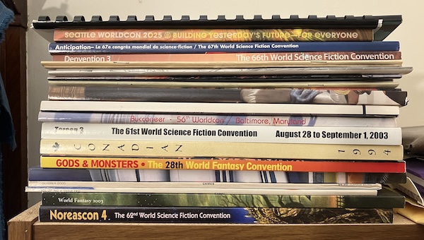 A stack of colorful perfect-bound booklets commemorating Worldcons. They include "Seattle Worldcon 2025", "Anticipation", "Denvention 3", "Bucconeer", "Torcon 3", "Conadian", and "Noreascon 4". Also visible are a couple of booklets from the World Fantasy Convention (it's different).