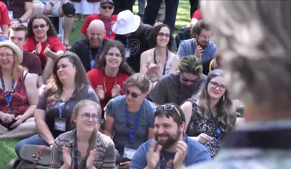 A view of Myst fans sitting on the lawn at the Cyan office. Rand Miller's head is visible in the foreground, out of focus. He must have said something good because people are applauding.