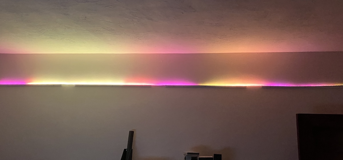 An LED strip runs along the top of a wall. The strip glows in irregular segments of yellow, orange, and magenta.