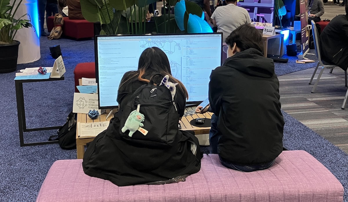 Two people sitting in front of Visible Zork 1. They are facing away from us and peering attentively at the screen.